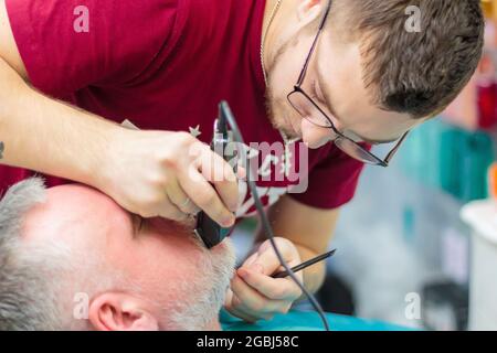 Der Meister schabt den Schnurrbart eines erwachsenen Mannes mit einer Schreibmaschine. Friseurservice-Konzept. Moskau, Russland 17. November 2016 Stockfoto