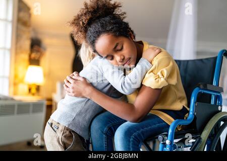 Schwarzes kleines Mädchen mit Behinderung im Rollstuhl, das sich mit ihrem jüngeren Bruder umarmt. Stockfoto