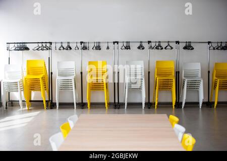 Reihen von weißen und gelben Plastikstühlen an einer weißen Wand in einem leeren Büro. Leerer Tagungsraum. Stockfoto