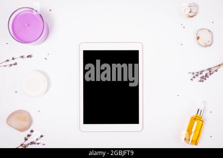 Tablet-pc mit leerem Bildschirm zwischen Naturkosmetik-Spa-Produkten, Steinen, Lavendelblüten und Kerze, Draufsicht. Stockfoto