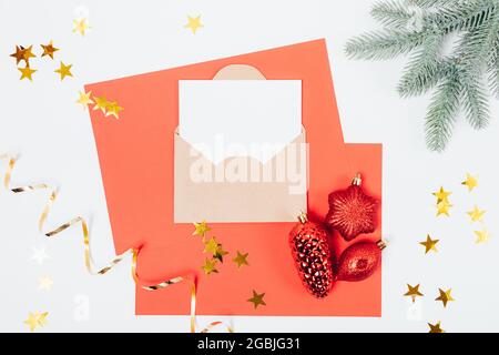 Weihnachtskartenschablone auf rotem Papier mit grünen Fichtenzweigen und weihnachtsbaumschmuck, flach aufgelegt. Stockfoto