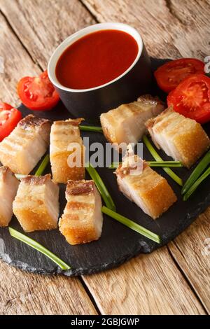 Lechon Kawali oder knusprig frittierter Schweinebauch mit süßer und saurer Sauce in der Schieferteller auf dem Tisch serviert. Vertikal Stockfoto