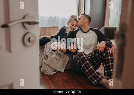 Feier des bewegenden Tages. Das Ehepaar Yong zieht in ein neues Zuhause. Junges glückliches Paar, frisch verheiratetes Familienmitglied, das Wein trinkt und Spaß im Zimmer mit Kartons hat Stockfoto