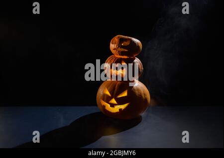 Eine gruselige Pyramide aus Jack-o-Laterne im Dunkeln. Glühender gruseliger Grinsen in einem Kürbis. Traditionelle halloween-Dekorationen. Horizontale Grußkarte Stockfoto