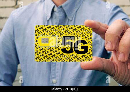 Ein Mann hält eine gelbe SIM-Karte mit der Aufschrift 5G für Mobiltelefon in der Hand. Austauschen der SIM-Karte und Umschalten auf Highspeed-Internet. Stockfoto