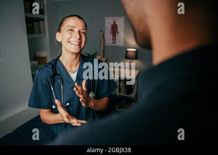 Kaukasische Krankenschwester steht lächelnd und plaudert mit einem männlichen Patienten Stockfoto