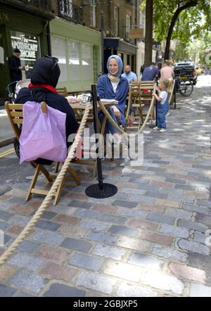 London, England, Großbritannien. Zwei Frauen mit Kopftüchern sitzen an einem Tisch vor einem Café während der COVID, Juli 2021 Stockfoto