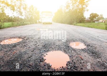 Eine holprige, nasse Schotterstraße nach dem Regen. Eine Schotterstraße ist voller Schlaglöcher. Eine Landstraße in Südkambodschan. Fokus auf Schlagloch im Vordergrund. Stockfoto