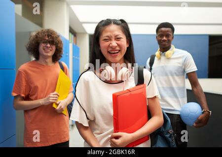 Porträt von drei Schülern verschiedener Rassen, die die Kamera anschauten und in der Schule lachten. Chinesisches Mädchen in der Schule mit ihren Klassenkameraden. Stockfoto