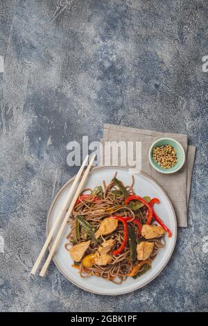 Japanische Gerichte Buchweizen Soba Nudeln mit Huhn und Gemüse Karotte, Paprika und grünen Bohnen in Wok auf dunkelblauem Hintergrund Stockfoto