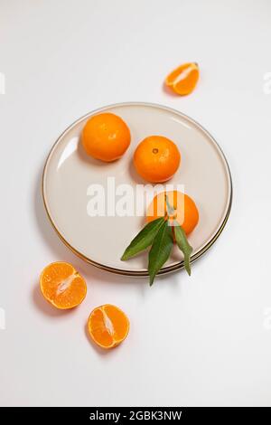 Frische Mandarinen- oder clementinfrüchte auf einem beigen Teller mit goldenem Rand auf weißem Grund. Farbenfroher Hintergrund mit Früchten. Dekorativer weihnachtsurlaub Stockfoto