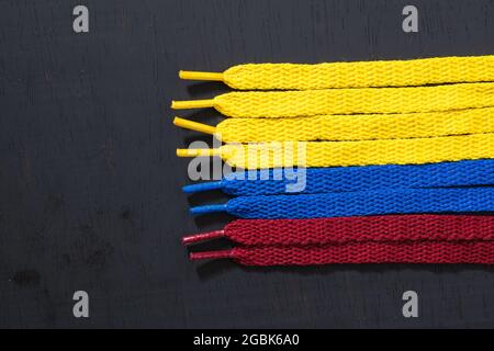 Hintergrund mit Flagge kolumbiens mit gelben, blauen und roten Schnürsenkeln, auf schwarzem Holz, vertikal angeordnet, Konzept der Perfektion, Stockfoto