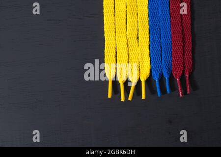 Hintergrund mit Flagge kolumbiens mit gelben, blauen und roten Schnürsenkeln, auf schwarzem Holz, vertikal angeordnet, Konzept der Perfektion, Stockfoto