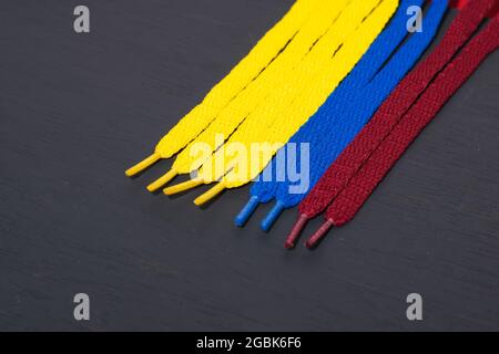 Hintergrund mit Flagge kolumbiens mit gelben, blauen und roten Schnürsenkeln, auf schwarzem Holz, vertikal angeordnet, Konzept der Perfektion, Stockfoto