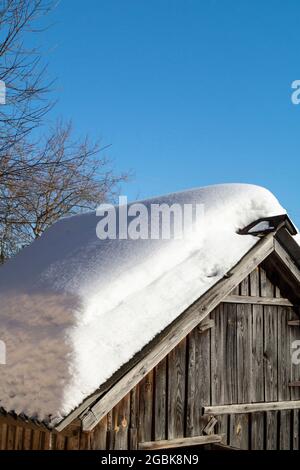 Schnee auf dem Dach eines Holzschuppens im Winter. Schönheit in der Natur an einem sonnigen Tag Stockfoto