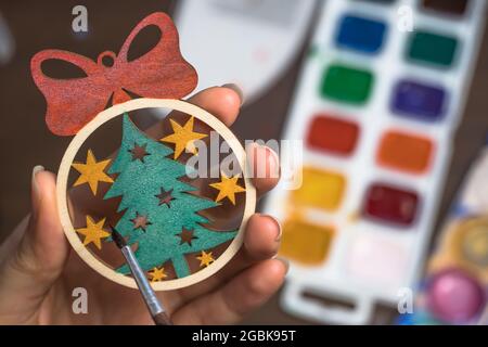 Bemalen Sie das Weihnachtsbaum-Spielzeug mit Farben. Gestalten Sie zu Hause eine Dekoration für das neue Jahr. Hobbys und Kreativität, handgefertigt. Der Künstler zeichnet auf ein Holz Stockfoto