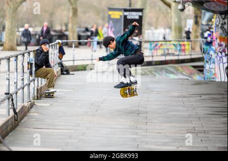 LONDON - 10. MÄRZ 2020: Skateboarder nutzt Smartphone, um seinen Freund auf einem Skateboard im Skatepark an der Londoner Themse South Bank zu drehen Stockfoto