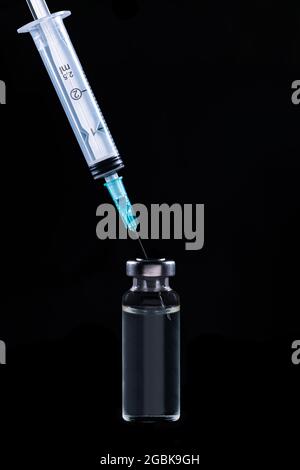 Große Vollimpffläschchen aus Glas und Spritze auf schwarzem Hintergrund Stockfoto