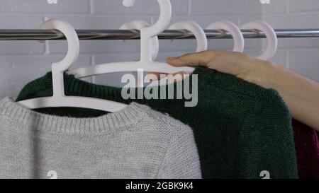 Der Verkäufer stellte Kleiderbügel an das Regal. Hängen Sie die Kleidung an einen Kleiderbügel. Strickpullover an Kleiderbügeln. Kleidung Kaufen. Kleidung an Kleiderbügeln beim Einkaufen Stockfoto