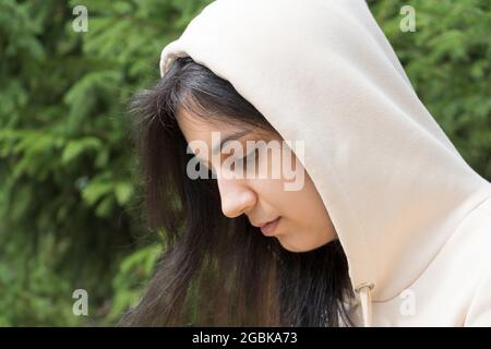 Die mit Kapuze versehene Brünette schaut nach unten. Das traurige Mädchen schaute herunter. Nahaufnahme eines schönen Mädchens in Depressionen. Schwermut, Opfer, Mobbing. Teen in casual out Stockfoto