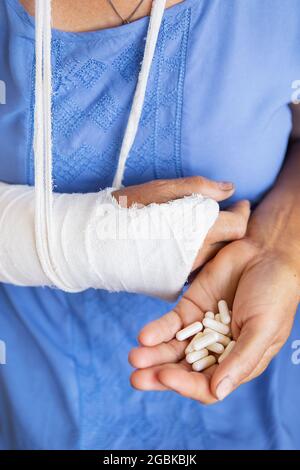 Eine ältere Frau im Ruhestand mit einem zurückgewickelten Arm in einem Guss und einem Verband hält Anäschetabletten. Schlag, Bruch, Knochen, Krankenhaus Stockfoto