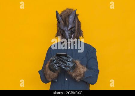 Auf einem gelben Hintergrund sieht man einen Werwolf, der in einem blauen Hemd gekleidet ist und den Touchscreen eines Smartphones berührt. Stockfoto