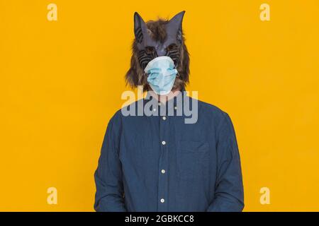 Auf einem gelben Hintergrund ist ein Werwolf in einem blauen Hemd mit einer OP-Maske gekleidet. Stockfoto