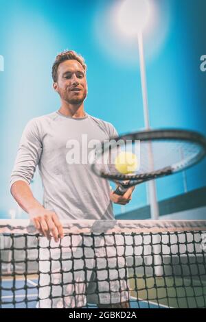 Mann Athlet Tennisspieler spielt auf dem Platz in der Nacht. Portrait am Netz mit Tennisschläger und Ball Stockfoto