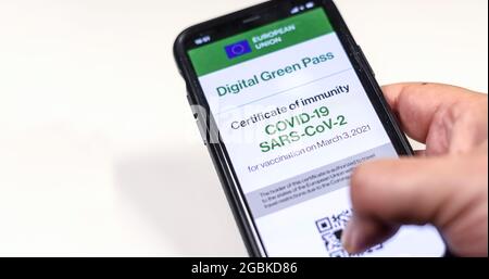 Der digitale grüne Pass der europäischen Union mit dem QR-Code auf dem Bildschirm eines Mobiltelefons, das von einer Hand auf weißem Hintergrund gehalten wird. Immunität gegen Covid-19. Stockfoto