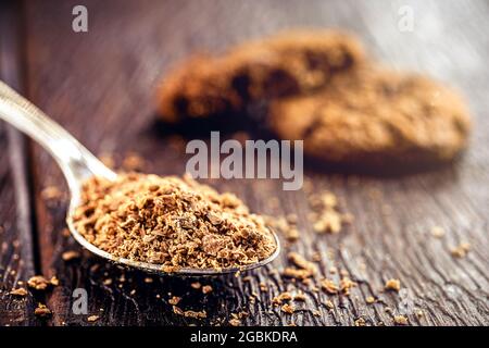 Löffel mit geriebener und dunkler Schokolade, Schokoladenpulver als Füllung für Süßigkeiten verwendet. Amerikanische hausgemachte Schokoladenkekse im Hintergrund Stockfoto