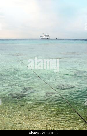 Fernsicht auf das Kreuzschiff Amadea, das in einer Lagune vor der Insel Tuamotu mit einem Festmacherseil, der zum Schiff führt, festgemacht ist Stockfoto