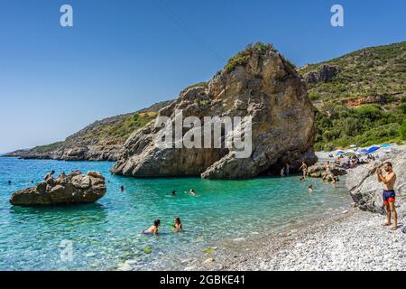 Panoramablick auf Foneas Strand überfüllt mit Touristen und Schwimmern. Der felsige Strand befindet sich in der Küstenregion Mani in der Nähe des Dorfes Kardamyli in M Stockfoto