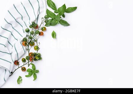 Frische Kirschtomatenzweige, Basilikumblätter, Serviette, Pfeffer- und Pfeffermühle auf weißem Hintergrund. Food Kochen Hintergrund und Mock up. Stockfoto