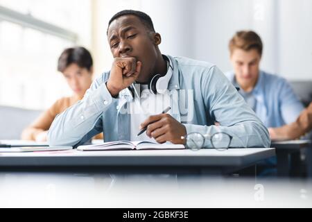 Schwarzer männlicher Student, der im Unterricht am Schreibtisch sitzt Stockfoto