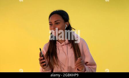 Fröhliches afrikanisches Mädchen, das die Musik in kabellosen Kopfhörern auf gelbem Hintergrund hört. Sie ist melomaniac. Stockfoto
