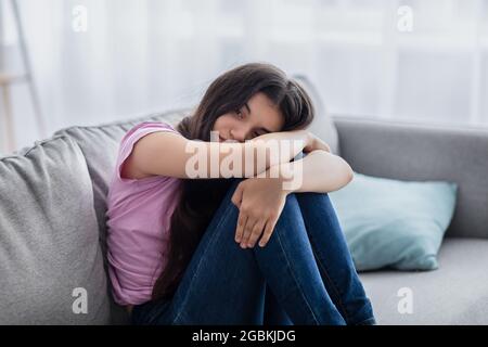 Unglückliches Teenager-Mädchen, das sich deprimiert oder verzweifelt fühlt, zu Hause auf der Couch sitzt, an Problemen oder Depressionen im Teenageralter leidet Stockfoto