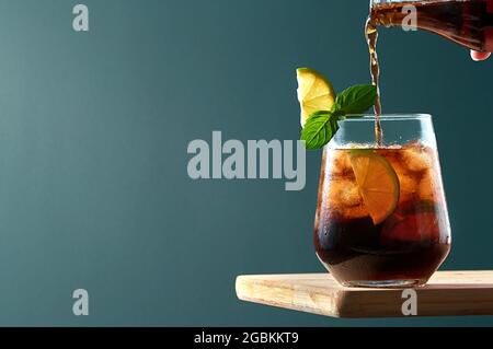 Cuba Libre oder Long Island Cocktail mit Cola, Rum und Limette in Glas auf Holzbrett mit dunkelblauem Hintergrund. Erfrischender Sommerdrink. Stockfoto