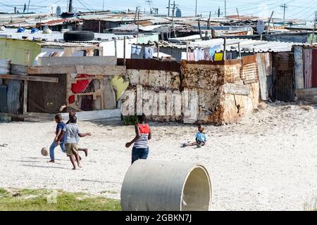 In den Blechhütten in einer afrikanischen Township, in der Kinder auf dem Sand in Kapstadt, Südafrika, Fußball spielen, wird das tägliche Leben in Afrika vorgestellt Stockfoto