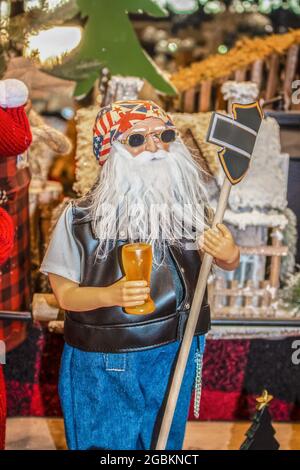 Biker Santa Figur mit Sonnenbrille und einem Bier halten Schild vor dem Durcheinander von anderen weihnachtlichen Gegenständen Stockfoto
