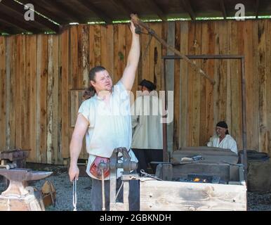 Der Schmied greift nach oben, um einen Hebel zu ziehen, um einen Blasebalg in der altmodischen Schmiede in der Renassiance Faire Muskogee Oklahoma USA zu betreiben Mai 22 2010 Stockfoto