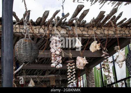 Nahaufnahme eines rustikalen Stockdachs in Mexiko mit Muscheln und geflochtenen Körben, die an alten Seilen und rostigen Ketten mit Kakteen draußen an den Enden der Stäbe hängen Stockfoto