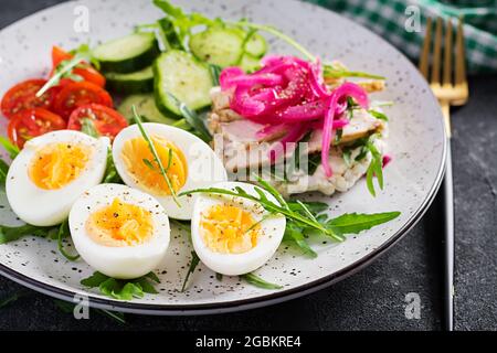 Frühstück. Gekochter Eiersalat mit Gemüse, Gurken, Tomaten und Sandwich mit Ricotta-Käse, gebratenem Hühnerfilet und roter Zwiebel. Keto/Paleo Mittagessen. Stockfoto