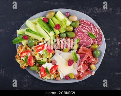 Charcuterie-Board. Platte: parmesan mit Prosciutto, Salami, Gurken und Oliven. Auswahl an leckeren Vorspeisen oder Antipasti. Draufsicht, Kopierbereich, Stockfoto