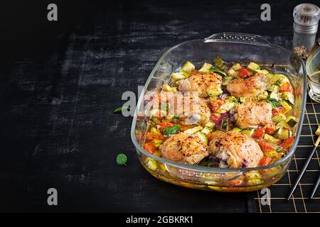 Gebackene Hähnchenschenkel, Zucchini und Gemüse in einer Auflaufform auf einem dunklen Tisch. Stockfoto