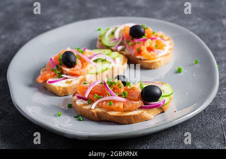 Toast mit Frischkäse, geräuchertem Lachs, Gurke, schwarzen Oliven und roten Zwiebeln. Offene Sandwiches. Gesunde Pflege, super-Food-Konzept. Stockfoto