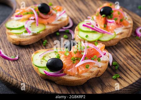 Toast mit Frischkäse, geräuchertem Lachs, Gurke und roter Zwiebel auf dunklem Tisch. Offene Sandwiches. Gesunde Pflege, super-Food-Konzept. Stockfoto