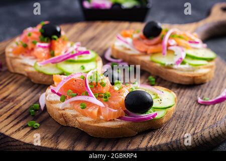 Toast mit Frischkäse, geräuchertem Lachs, Gurke und roter Zwiebel auf dunklem Tisch. Offene Sandwiches. Gesunde Pflege, super-Food-Konzept. Stockfoto