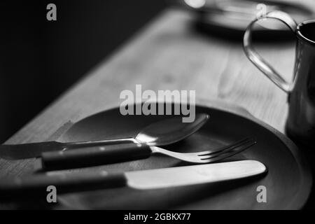 Trio. Löffel, Gabel und Messer in der Holzplatte. Unschärfer Schwarzweiß-Hintergrund. Nahaufnahme. Stockfoto