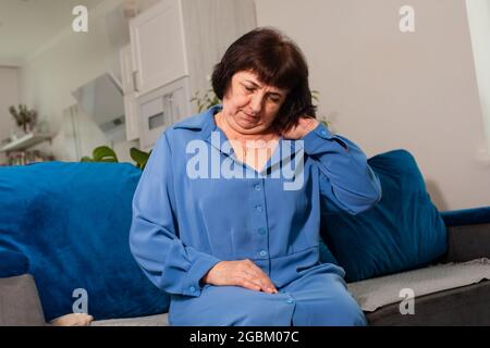 Ältere Frau im blauen Hemd, die unter Nackenschmerzen leidet Stockfoto