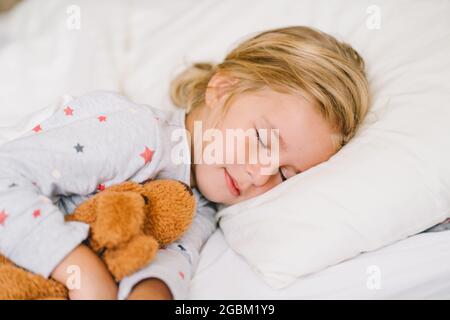 Kleinkind Mädchen im Schlafanzug schlafen auf weißen Bettwäsche und Umarmung Plüsch Spielzeug Stockfoto